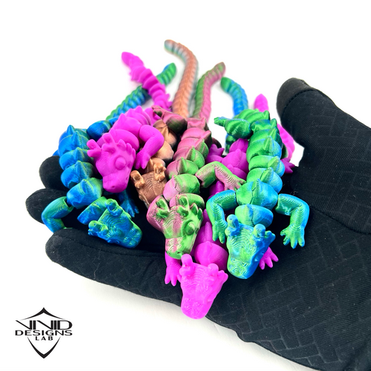3D printed toy dragons in hand with white backdrop, many colorful dragons