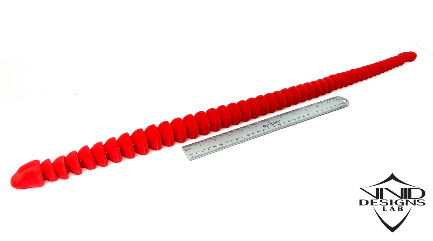 3D printed red articulated toy snake next to ruler with white background