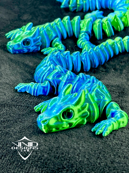 A toy dragon with blue and green colors, featuring a smooth, shiny texture and detailed face and body design. 3D printed bone dragons on black fabric.